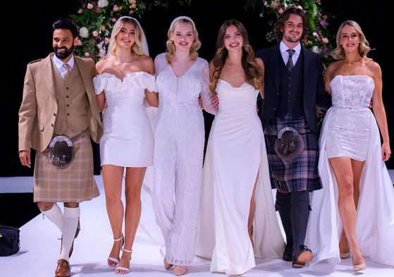 Group of men in kilts and women in wedding dresses standing next to each other 